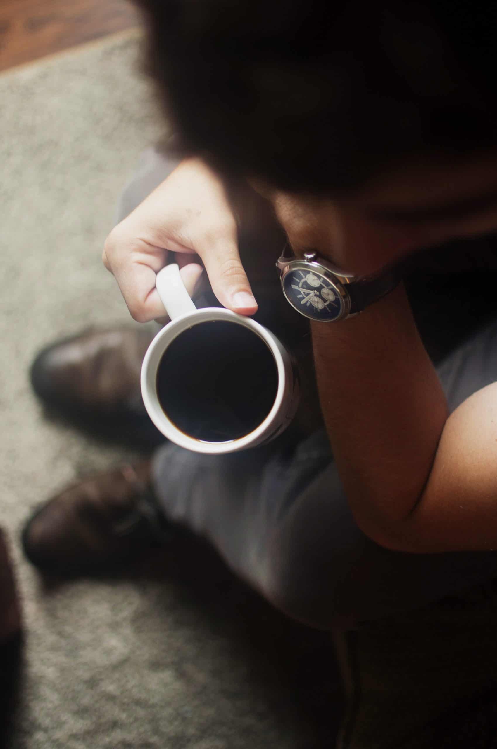 blurred person bending over a cup of black coffee