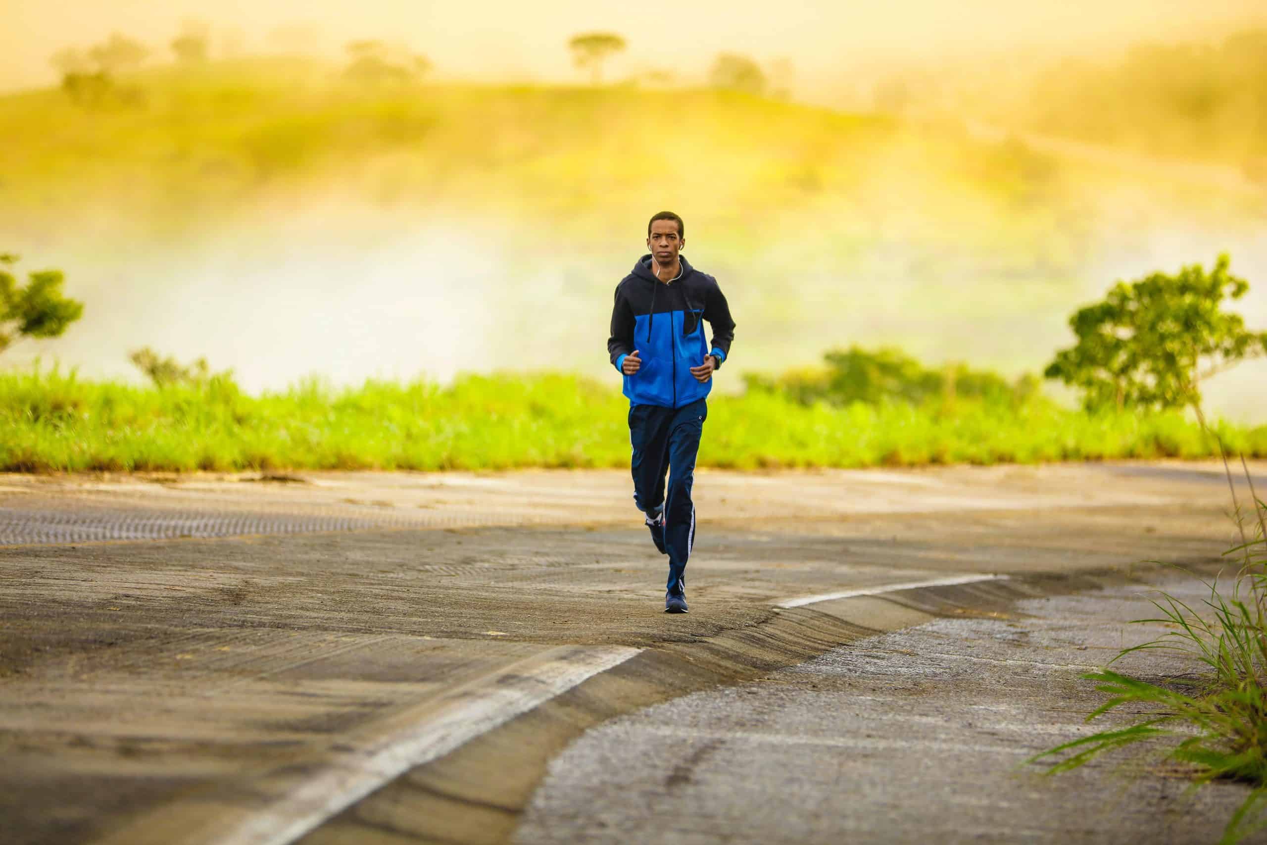 man running on a road, wearing a blue tracksuit, yellow sunlight behind him