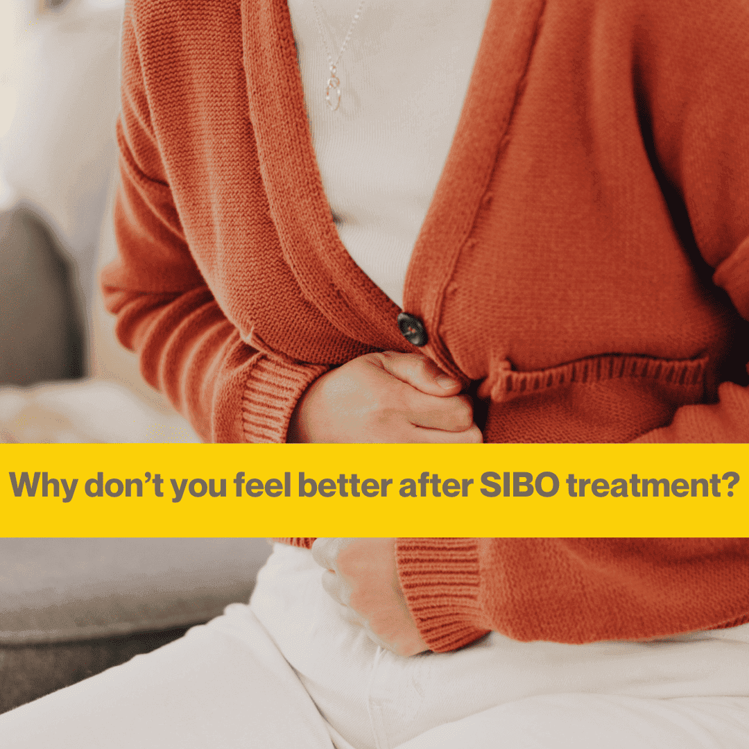 Woman's torso close up. She is wearing an amber cardigan and white T shirt, white trousers. She is clutching her stomach. The words Why you don't feel better after SIBO treatment.