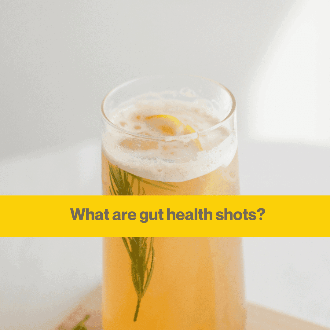 Glass containing some orangey yellow liquid and a sprig of rosemary. The background is a white wall with sunlight in the coner.