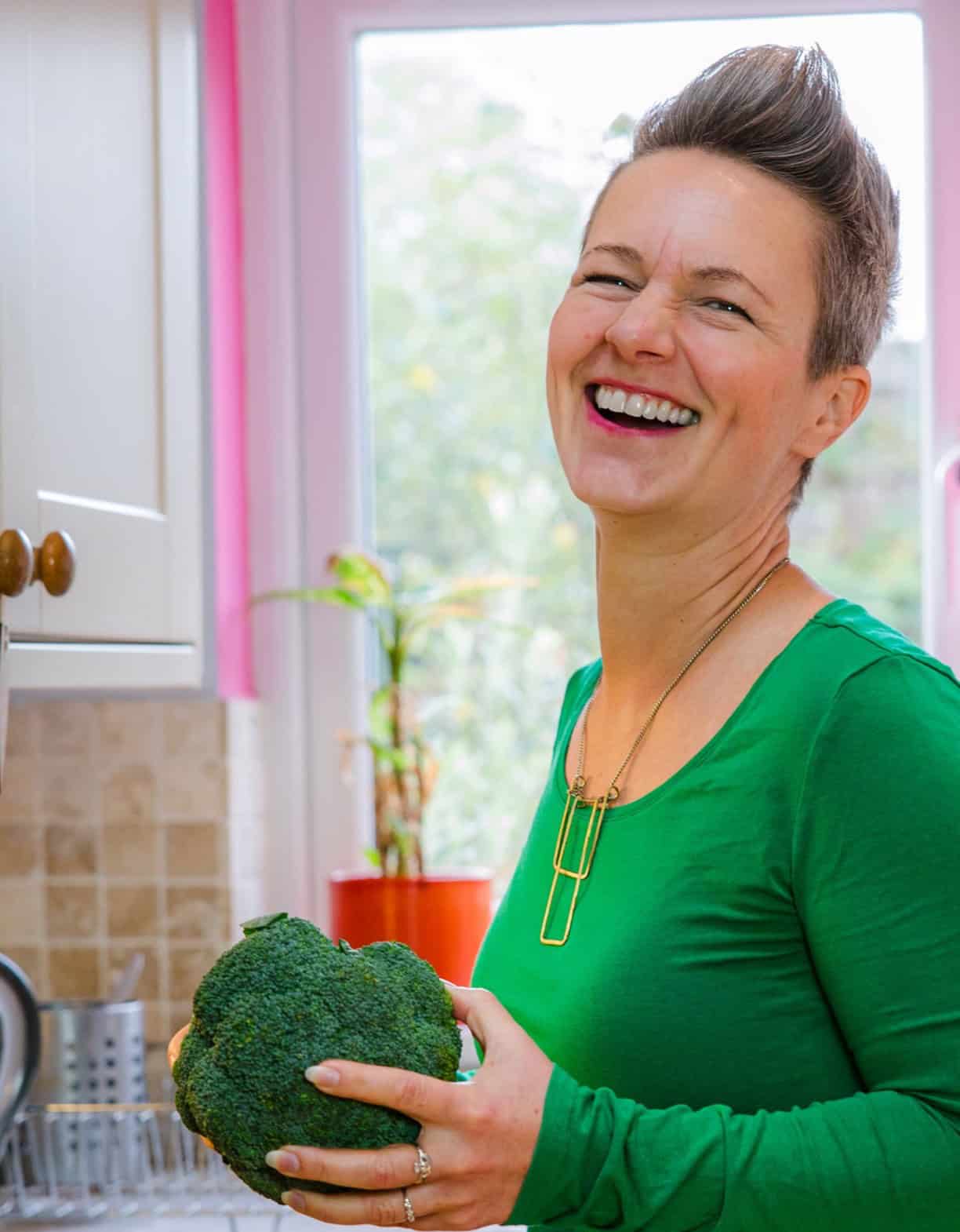 Nutritionist reviewing a meal plan with a man seated at a table, with fruits, a clipboard, and healthy food items visible in a bright kitchen setting.