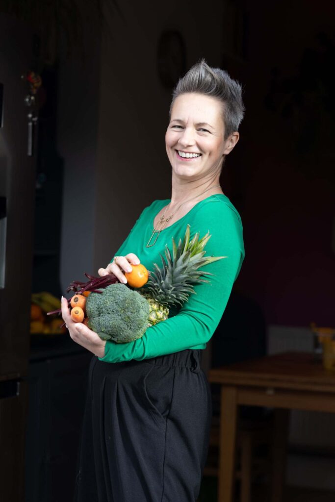 Nutritionist reviewing a meal plan with a man seated at a table, with fruits, a clipboard, and healthy food items visible in a bright kitchen setting.