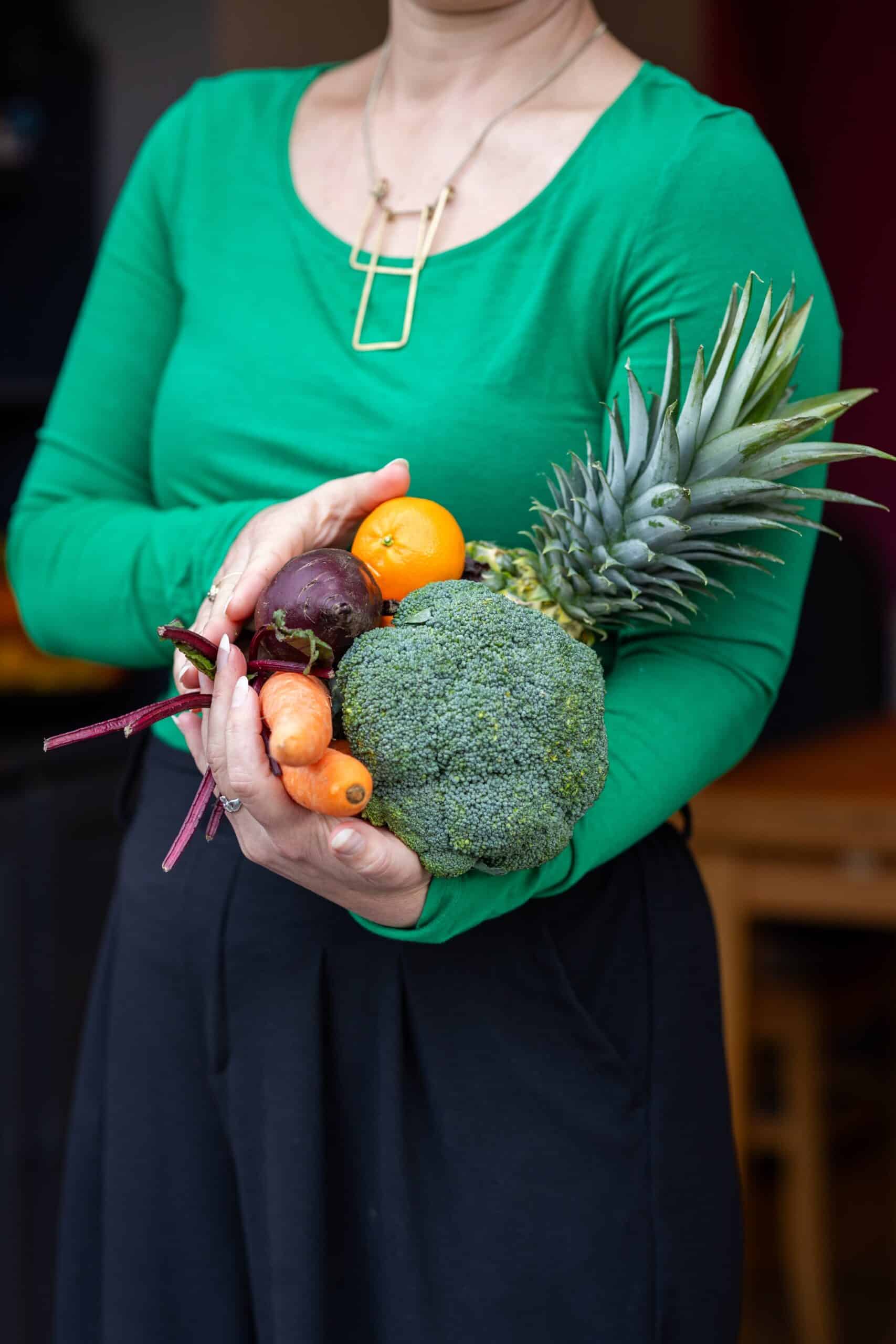 Nutritionist reviewing a meal plan with a man seated at a table, with fruits, a clipboard, and healthy food items visible in a bright kitchen setting.