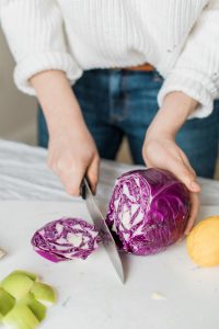 Nutritionist reviewing a meal plan with a man seated at a table, with fruits, a clipboard, and healthy food items visible in a bright kitchen setting.
