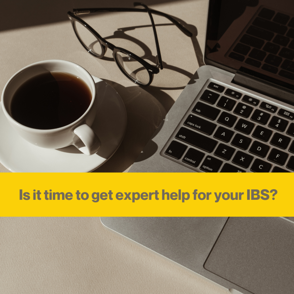 Grey laptop and a white coffee cup next to it. Glasses on the table creating a shadow in the sunlight. Words Is it time to get expert help for your IBS